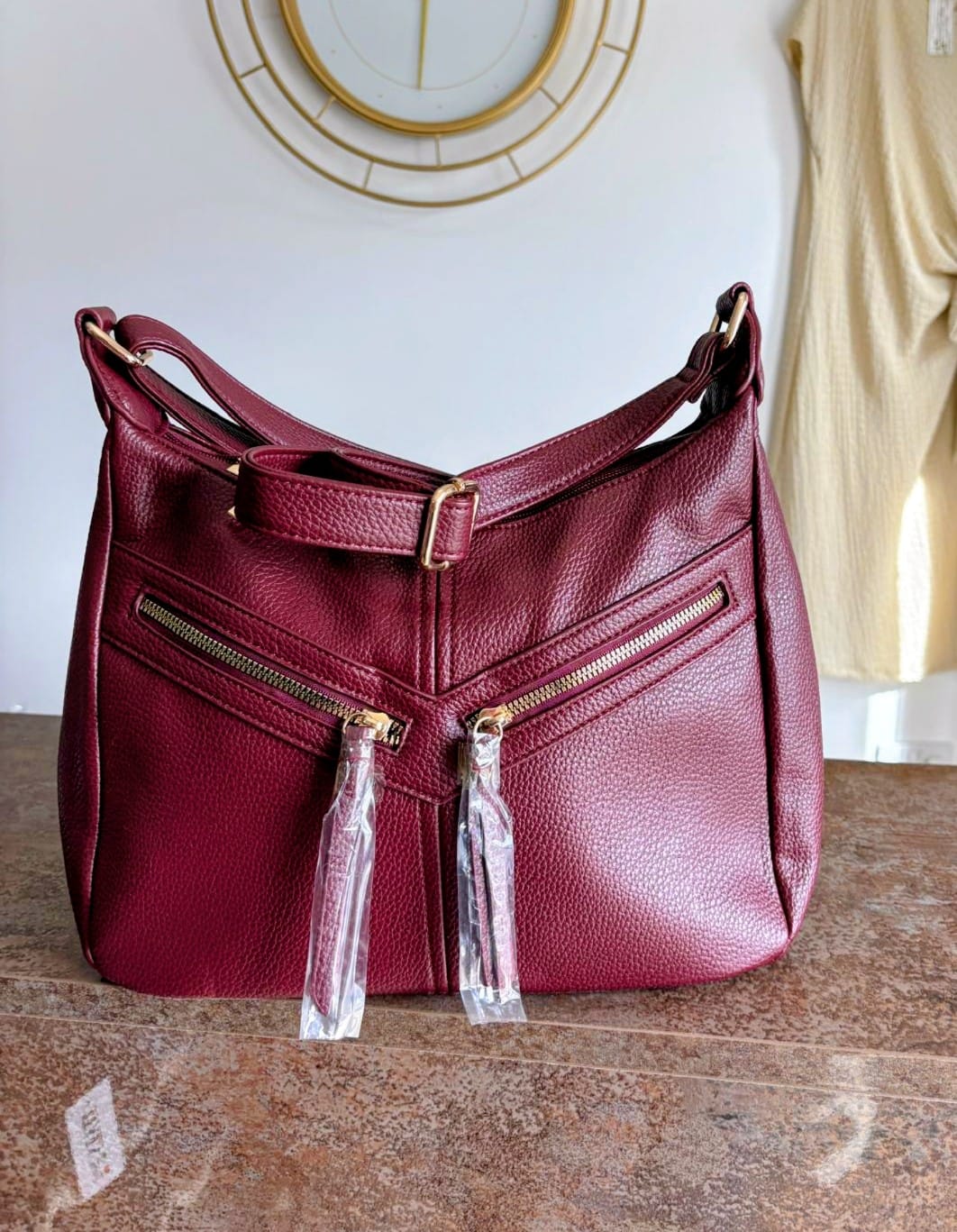 Maroon handbag with gold zippers on a wooden surface