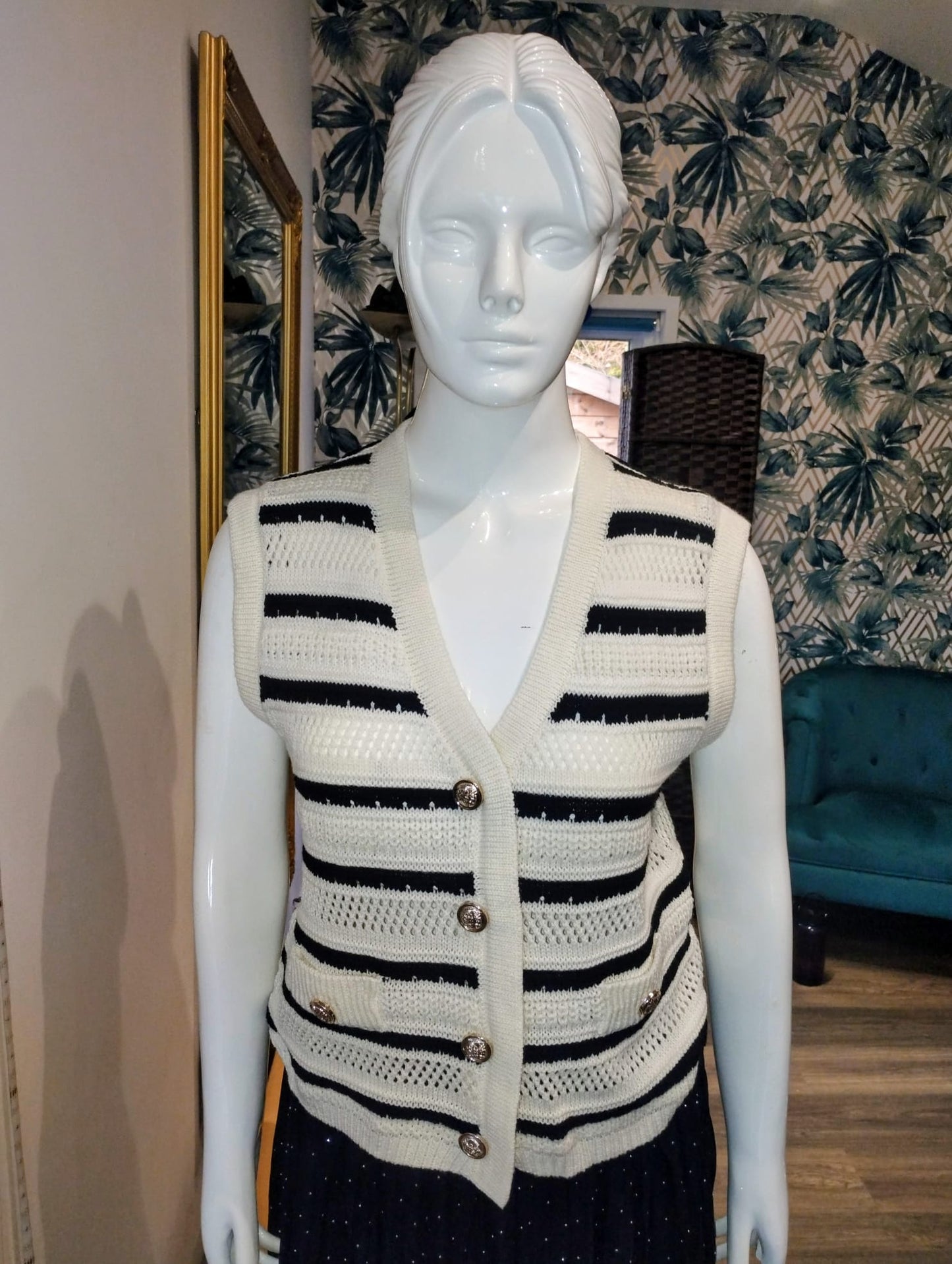Mannequin wearing a black and white striped sweater in a room with patterned wallpaper.