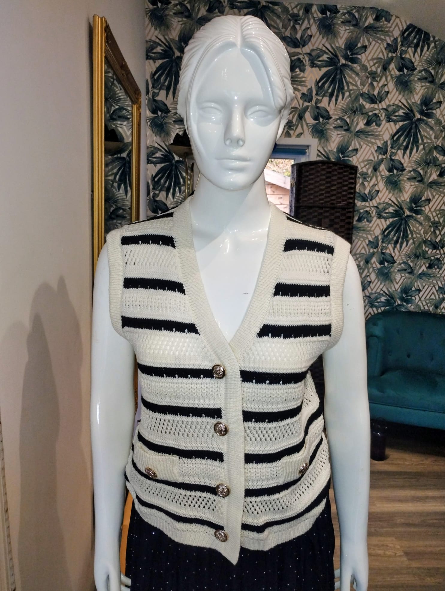 Mannequin wearing a black and white striped sweater in a room with patterned wallpaper.