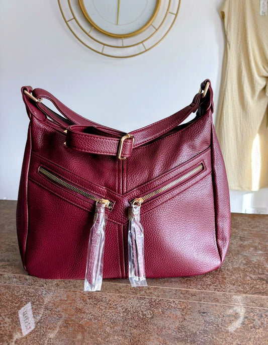 Maroon handbag with gold zippers on a wooden surface