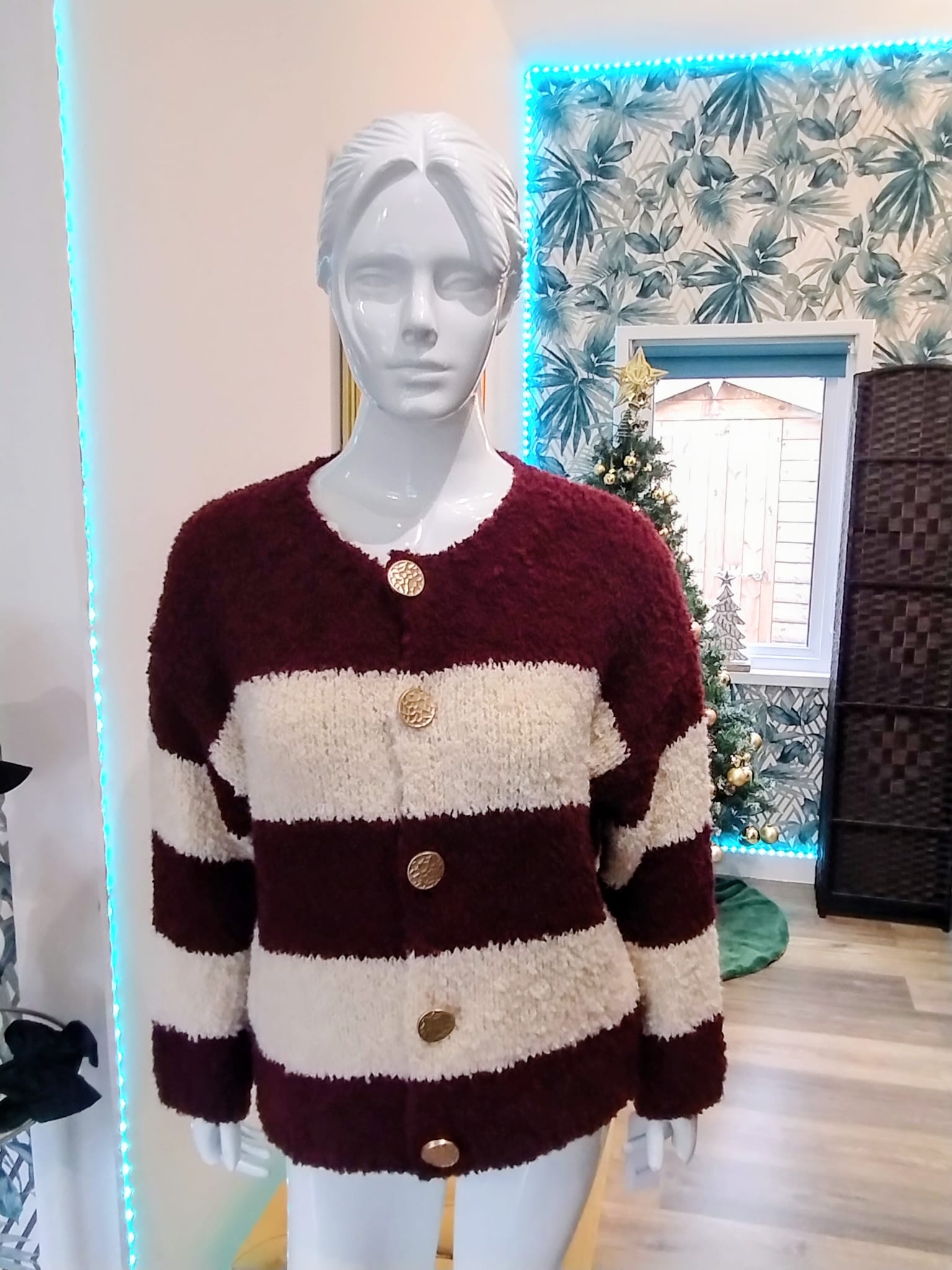 Mannequin wearing a maroon and beige striped sweater with buttons in a decorated room.