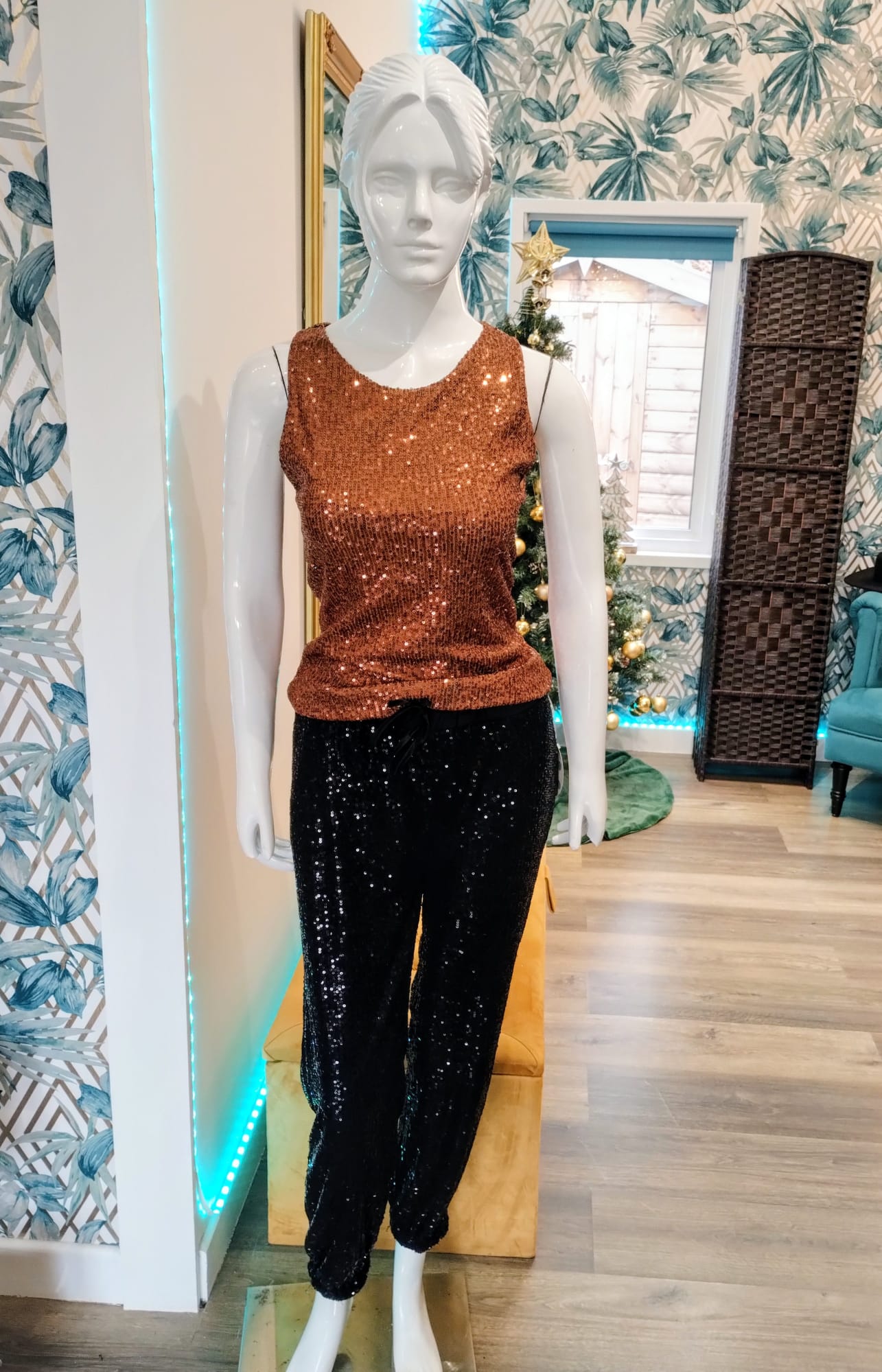 Mannequin wearing a brown sequin top and black sequin pants in a decorated room.