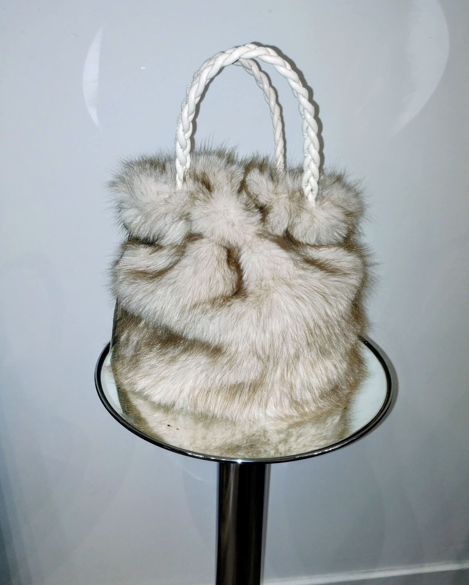 Fur handbag with braided handle on a stand against a plain background